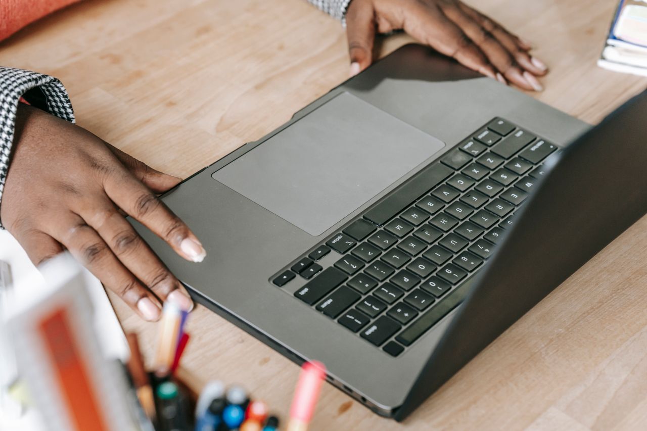 Vue de dessus d’une femme afro-américaine active et anonyme, travaillant en ligne sur un projet, installée à une table avec un netbook